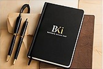 Notebook hitam dan dua pulpen dengan logo BKi